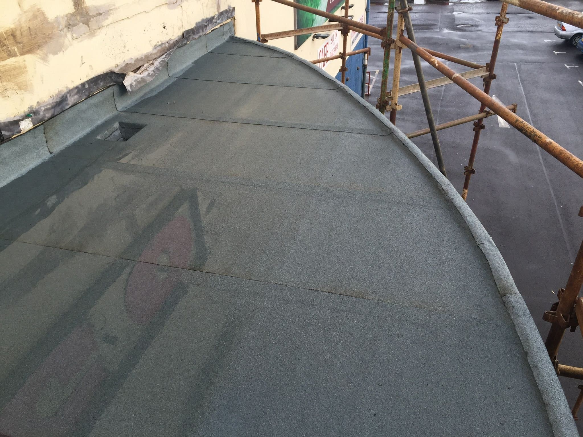 Newly felted flat roof edge on a commercial building, scaffolding alongside
