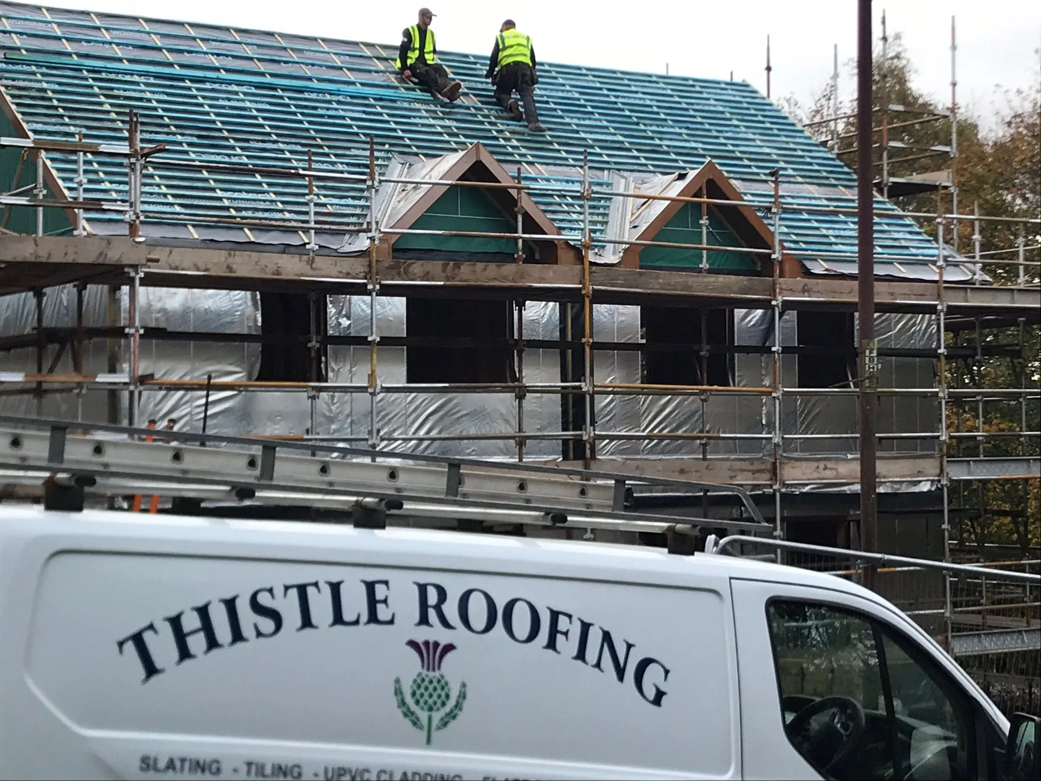 Thistle Roofing team fitting a new roof, with the company van parked below